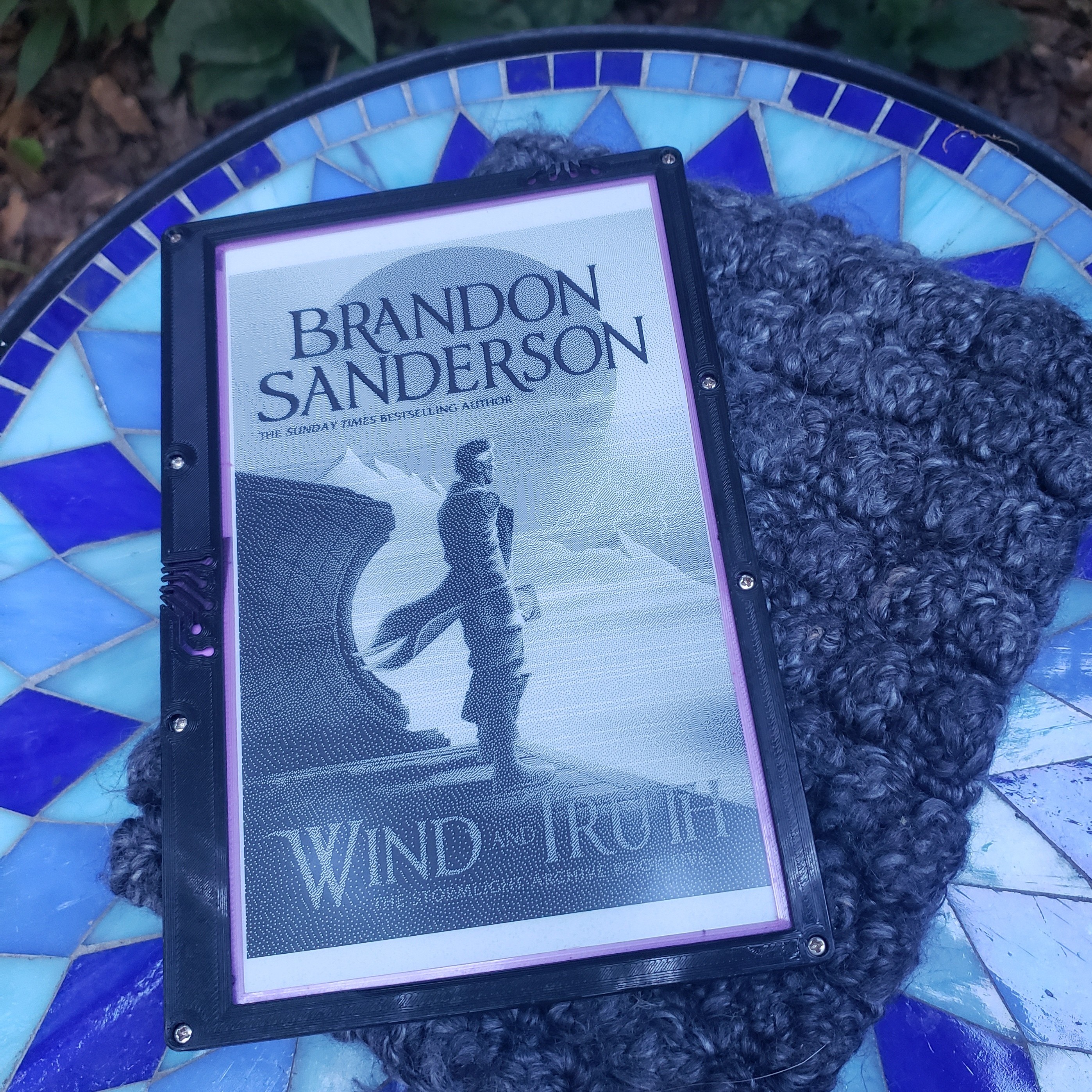 E-paper screen in a 3D-printed enclosure, displaying a black-and-white cover of "Wind and Truth" by Brandon Sanderson
