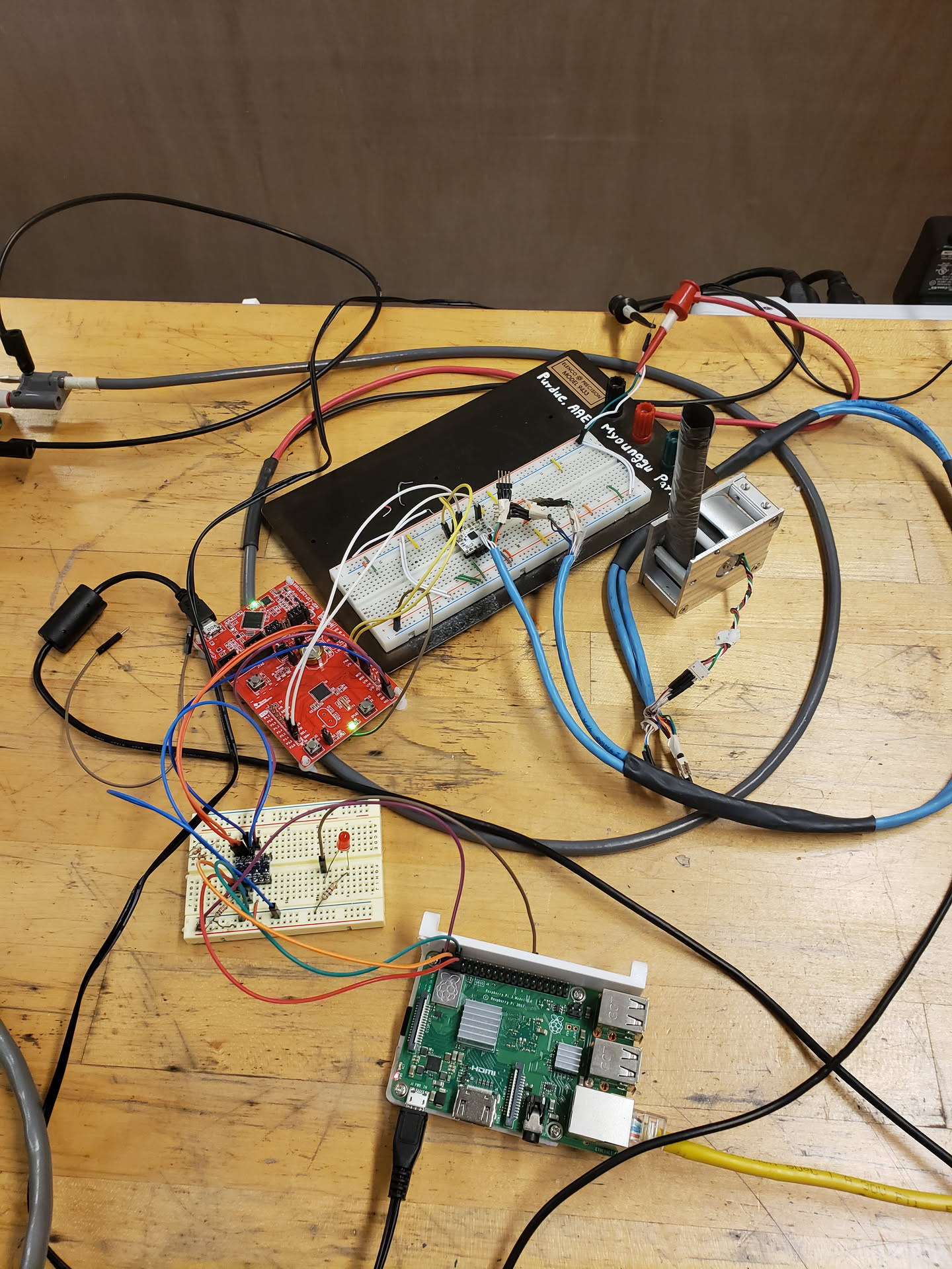 Wooden counter with a laptop, Raspberry Pi, breadboard, and development board for the microcontroller all wired together